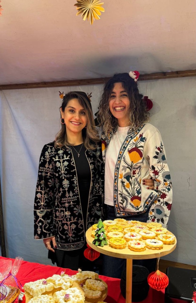 Zahra und Parnian lächelnd hinter ihrem Kekstisch auf einem Weihnachtsmarkt